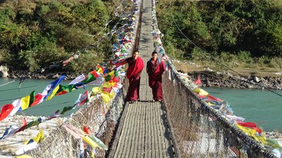 Zwei Mönche auf einer von Gebetsfahnen gezierten Hängebrücke bei Punakha