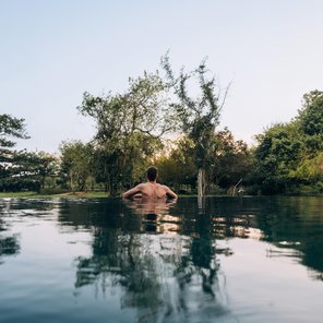 Mann im Pool schaut in die grüne Landschaft mit Bäumen