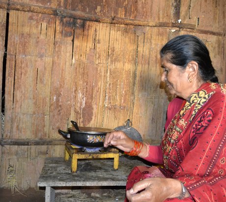 Frau in rot gekleidet vor einem Gaskocher mit einem Topf