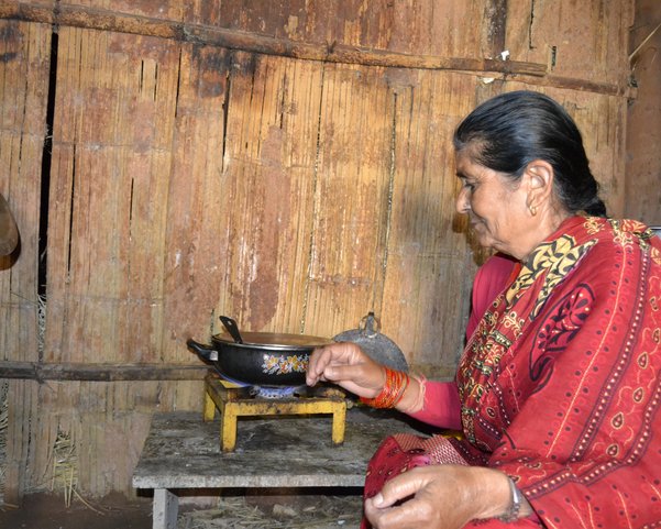 yoga-urlaub-nepal-frau-gasherd-kochtopf Frau in rot gekleidet vor einem Gaskocher mit einem Topf
