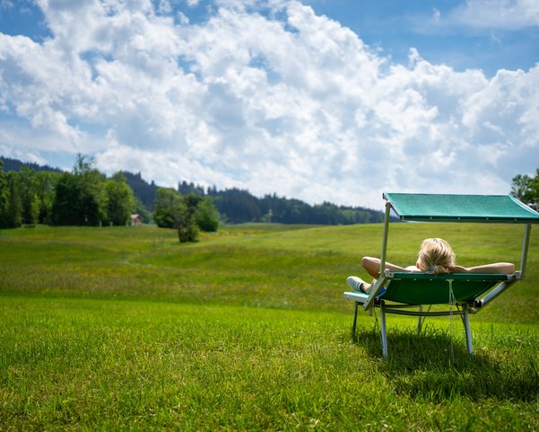 Eine Frau liegt auf einer grünen Weide und sonnt sich auf einer Sonnenliege