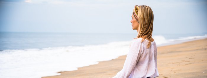 Eine blonde Frau meditiert im Schneidersitz am Strand