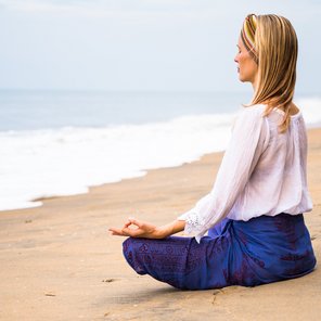 Eine blonde Frau meditiert im Schneidersitz am Strand