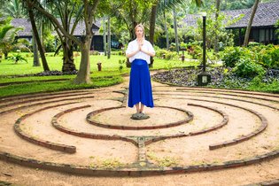 Eine Frau steht in einem Garten die Hände in anjali mudra
