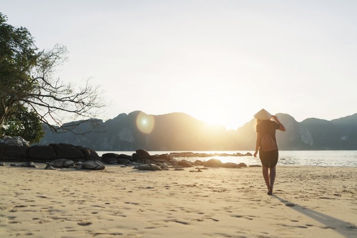 Eine Frau mit einem asiatischen Kegelhut spaziert am Strand