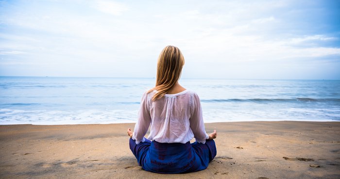 Eine blonde Frau übt Meditation an einem Strand