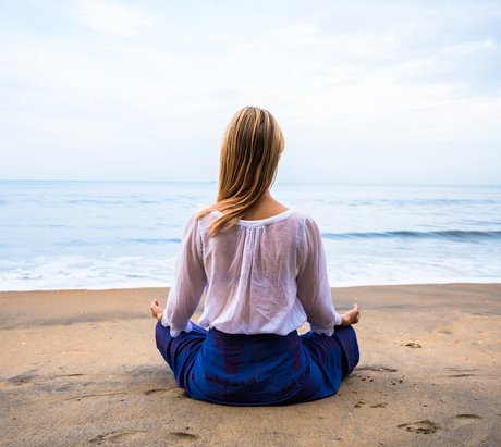 Eine blonde Frau übt Meditation an einem Strand