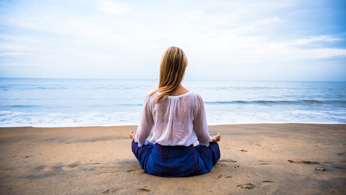 Eine blonde Frau übt Meditation an einem Strand