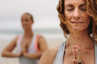 Ein Mann und eine Frau meditieren im stehen an einem Strand