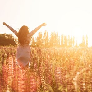 Glückliche Frau in grüner Blumenwiese hebt die Hände zum Himmel